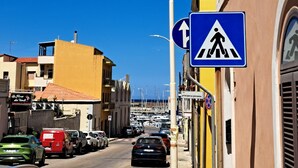 Una calle con coches estacionados, una señal de paso de peatones y edificios con balcones.