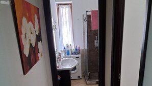 Un pasillo que conduce a un baño con lavamanos, ducha y suelo de baldosas.