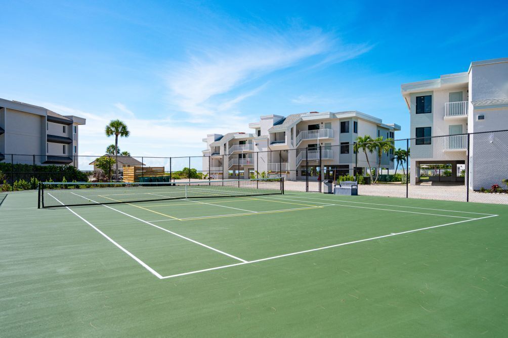 A tennis court with a net, surrounded by apartment buildings.