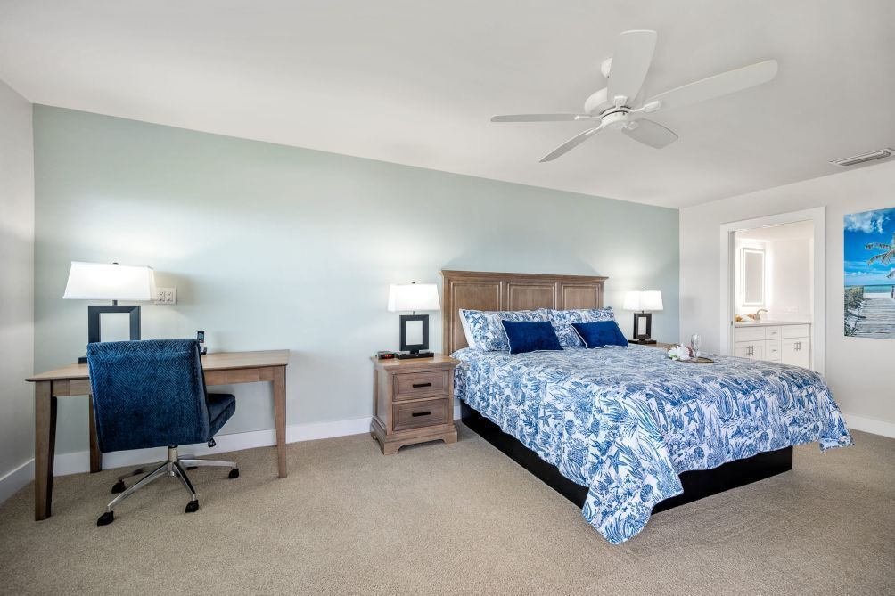 A bedroom with a bed, desk, chair, nightstands, and a ceiling fan.