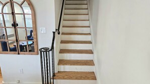 Una escalera con peldaños de madera y barandilla de metal, que lleva a un umbral oscuro.