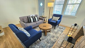 Una sala de estar con un sofá gris, sillones azules, una mesa de centro de madera y una chimenea de piedra.
