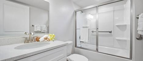 Un baño moderno con ducha envuelta en vidrio, un lavabo blanco con espejo y un inodoro.