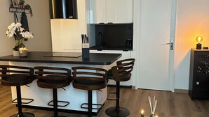 A modern kitchen with white cabinets, a black countertop, and a black stove. There are two wooden bar stools and a round table with candles. - Bright new T2 apartment next to the beach (Nice)