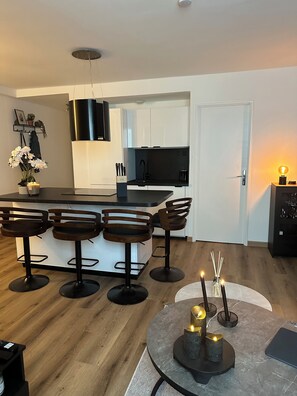 A modern kitchen with white cabinets, a black countertop, and a black stove. There are two wooden bar stools and a round table with candles. - Bright new T2 apartment next to the beach (Nice)