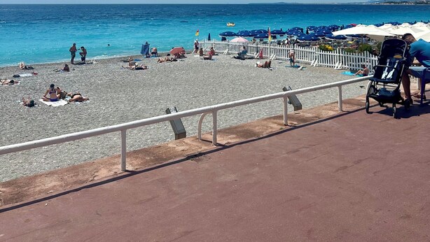 A beach with people sunbathing and a stroller, a white fence, and umbrellas. - Bright new T2 apartment next to the beach (Nice)