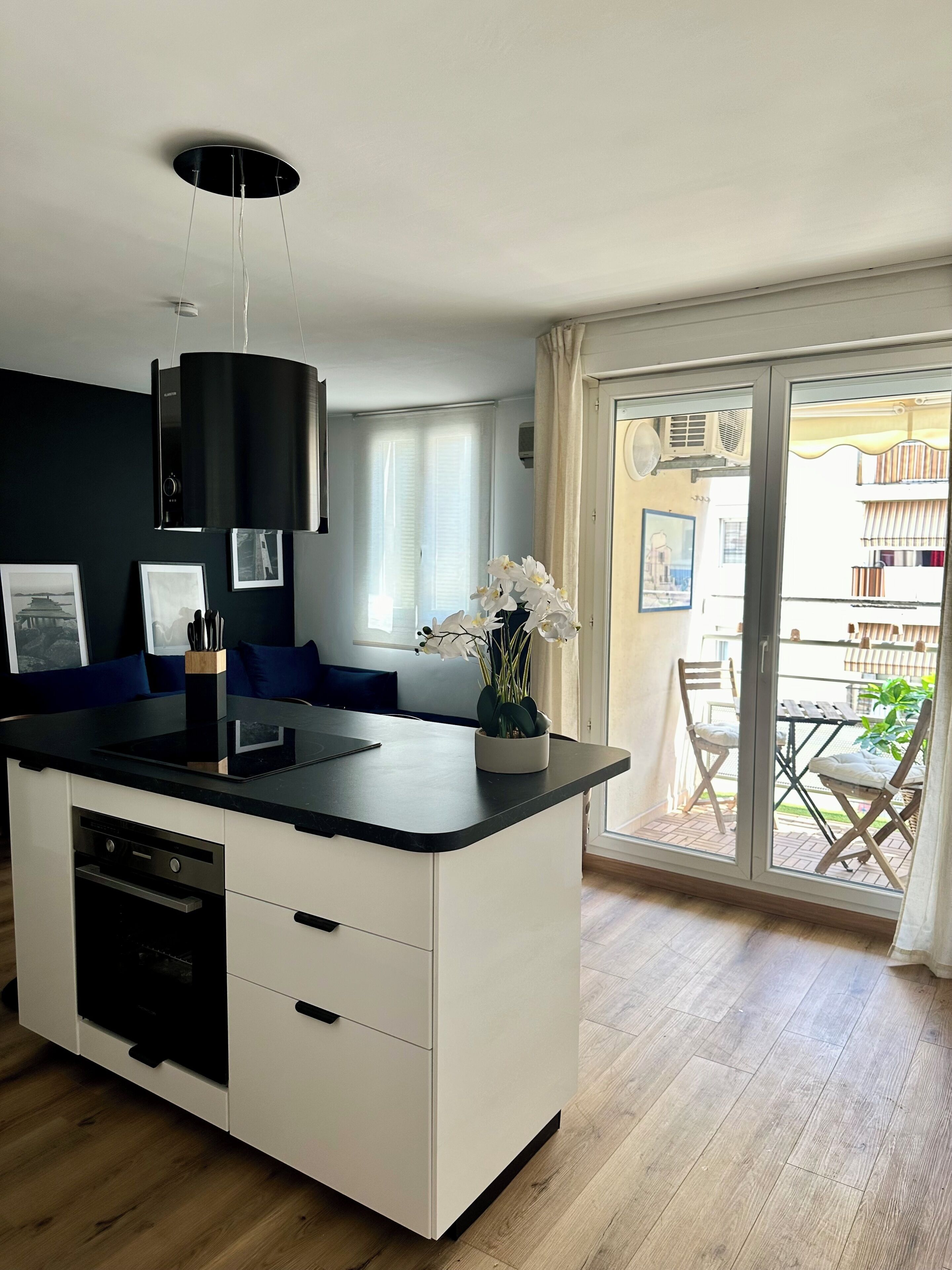 A modern kitchen with a central island, a dining area with a table and chairs, and a sliding glass door leading to an outdoor balcony.