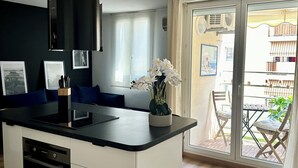 A modern kitchen with a central island, a dining area with a table and chairs, and a sliding glass door leading to an outdoor balcony. - Bright new T2 apartment next to the beach (Nice)