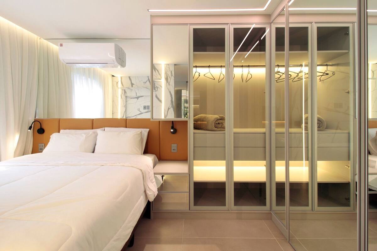 A modern hotel room with a bed, a walk-in closet with mirrors, and a wall-mounted air conditioner.