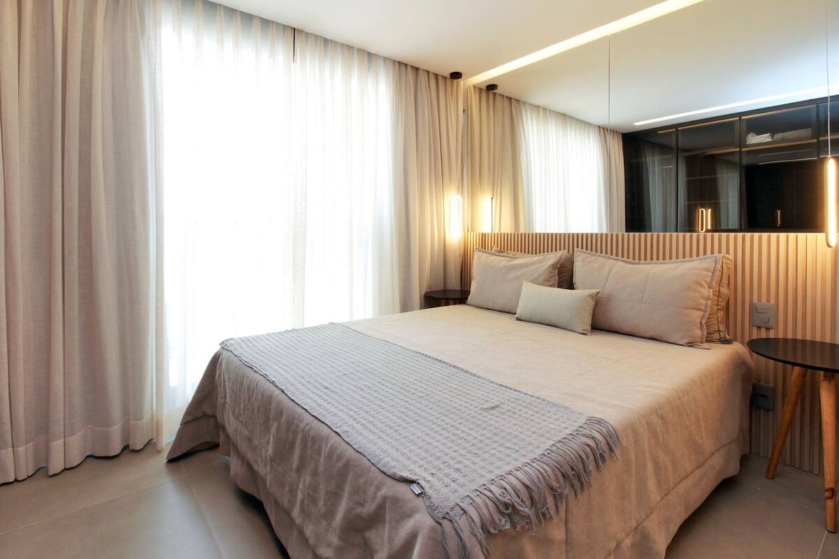 A modern hotel room with a large bed, a bedside table, and a mirror.