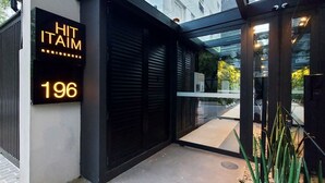 Ingresso di un edificio moderno con un'insegna al neon che riporta la scritta 'HIT IT AIM 196' e una porta in vetro che dà accesso all'interno.