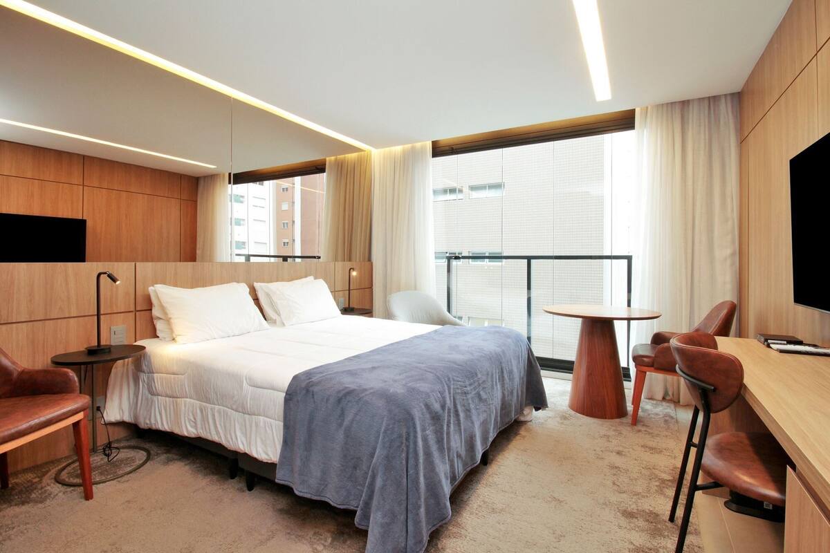 A hotel room with a bed, a desk, a chair, and a TV.