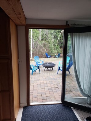 Una stanza con una porta scorrevole in vetro che dà su un patio esterno con sedie blu e un braciere.