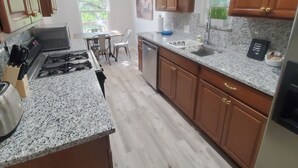 A kitchen with granite countertops, wooden cabinets, a gas stove, and a dining area with chairs and a table. - Soothing 3-bedroom house with AC in vibrant Austin near downtown! (Austin)