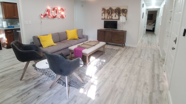 A modern living room with a sofa, chairs, a coffee table, a TV, and a ceiling fan. - Soothing 3-bedroom house with AC in vibrant Austin near downtown! (Austin)