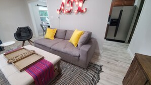 A living room with a sofa, a coffee table, a rug, and a wall-mounted light sign. - Soothing 3-bedroom house with AC in vibrant Austin near downtown! (Austin)