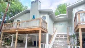 A two-story house with a wooden deck, a staircase, and a stone wall. - Soothing 3-bedroom house with AC in vibrant Austin near downtown! (Austin)