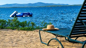 Une chaise de plage avec un chapeau de paille, un bateau gonflable bleu et des montagnes en arrière-plan.
