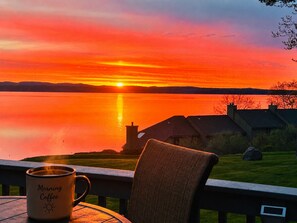 Vista al tramonto da un balcone con una tazza etichettata 'Morning Coffee' e una sedia.
