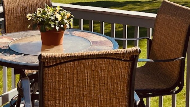 Un balcon avec des fauteuils en osier, une table ornée d’une plante en pot, et une vue sur la mer et les montagnes.