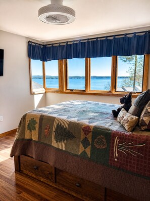 A bedroom with a large bed, a window with a view of a lake, and a ceiling fan. - Lake Winni Getaway I Steps to Beach+ Pool l Lake Views l Samoset (Gilford)