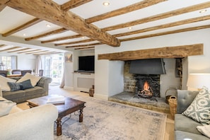 A living room with exposed wooden beams, a fireplace, sofas, and a television.