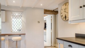Una cocina con un reloj de pared grande, una ventana con diseño de celosía y una puerta que da a otra habitación.