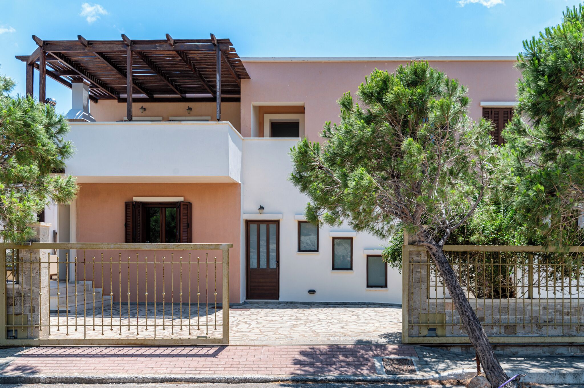 A modern two-story house with a wooden pergola, a gated entrance, and a paved driveway.