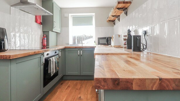A modern kitchen with a wooden countertop, built-in oven, and a window providing natural light. - Vasey Croft (Keighley)