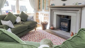 A cozy living room with a green sofa, a fireplace, and a large wall clock. - Vasey Croft (Keighley)