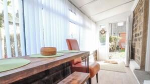 A wooden table with a bowl and placemats, a bench, and a chair in a room with a stone wall and a door leading outside. - Vasey Croft (Keighley)