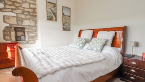 A bed with white bedding, two side tables, a wooden headboard, and a stone wall. - Vasey Croft (Keighley)