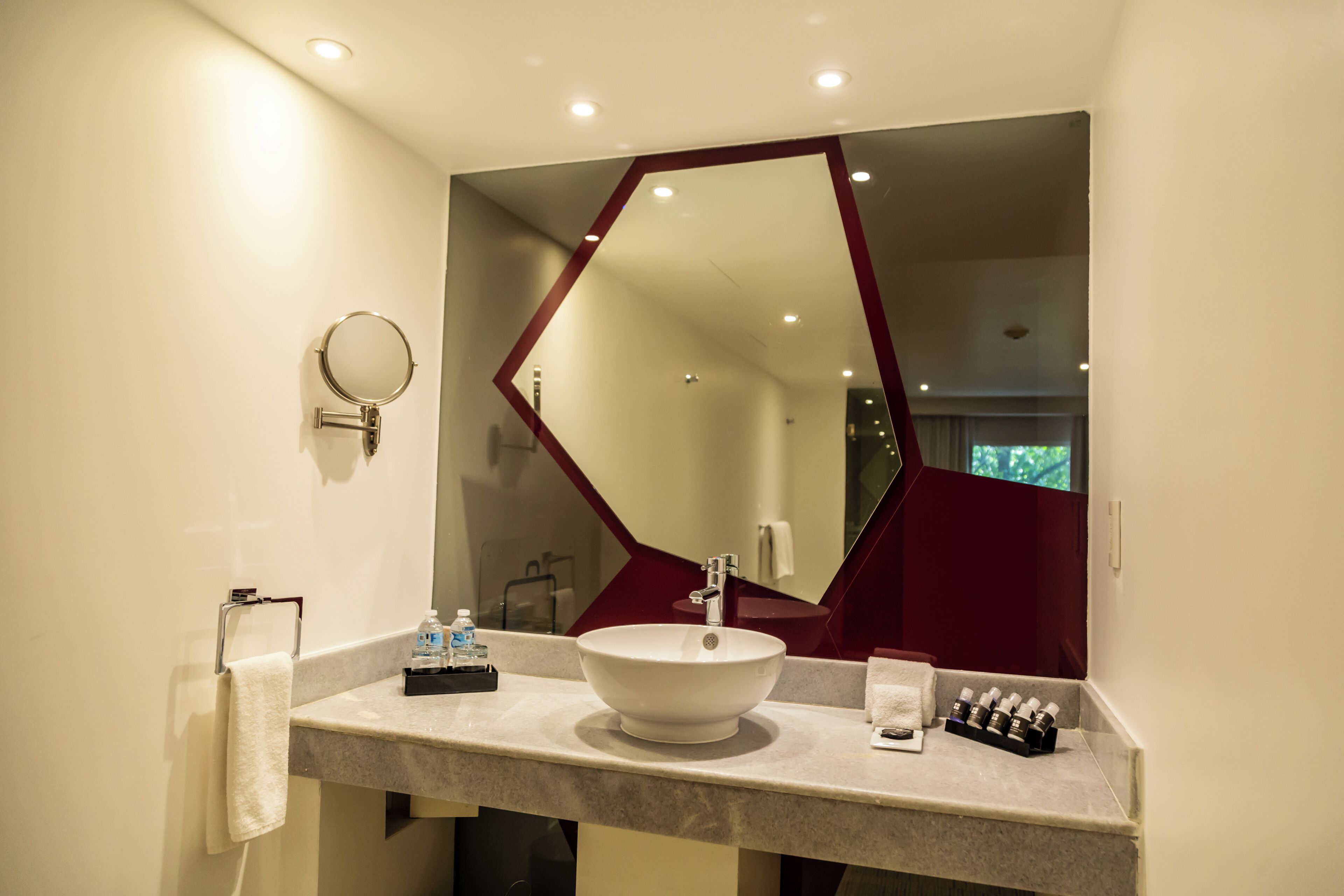 Un baño con un espejo redondo, un lavabo blanco y un espejo con marco rojo.