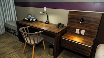 A hotel room with a wooden desk, a chair, a desk lamp, a telephone, and a small trash can.