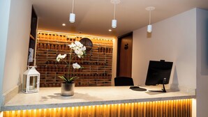 Mostrador de recepción con pared de madera, una orquídea en maceta, un farol blanco y un monitor de computadora.