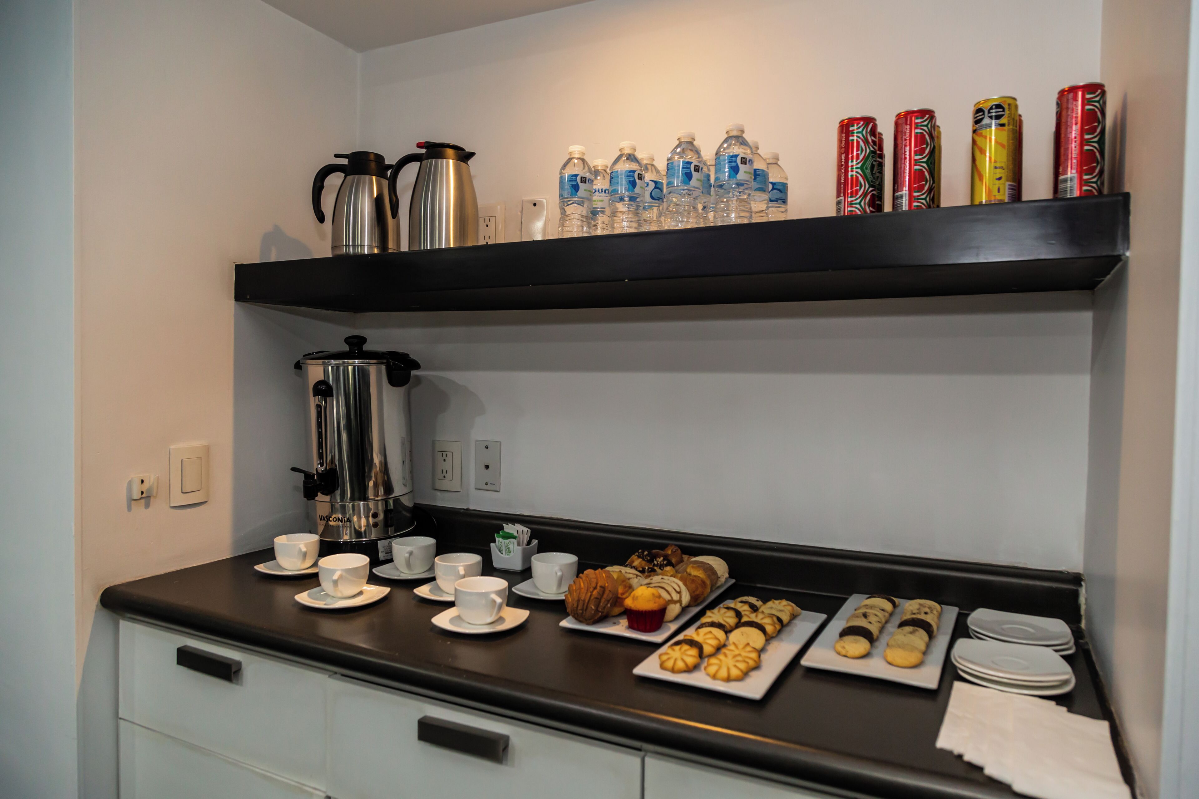 A breakfast buffet setup with coffee makers, water bottles, and various pastries on a counter.