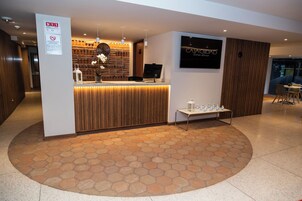 Un espace d’accueil d’hôtel avec un comptoir de réception en bois, une horloge et un panneau fixé au mur.