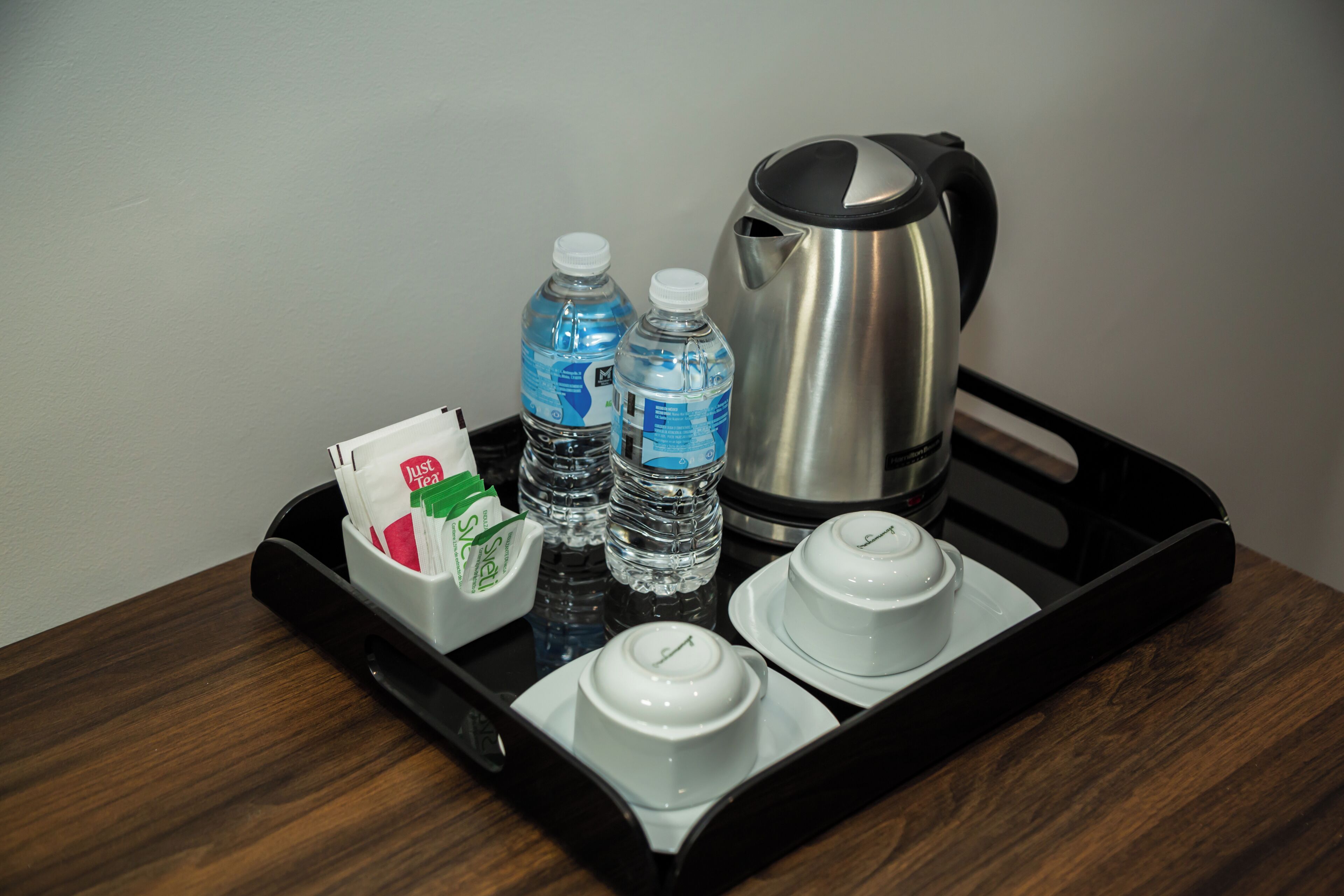 A tray with two water bottles, a coffee pot, and two white cups on a wooden table.