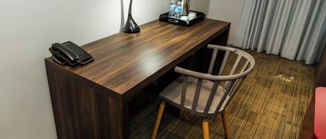 Habitación de hotel con escritorio de madera, teléfono, lámpara, silla y bandeja con cafetera y botellas de agua.
