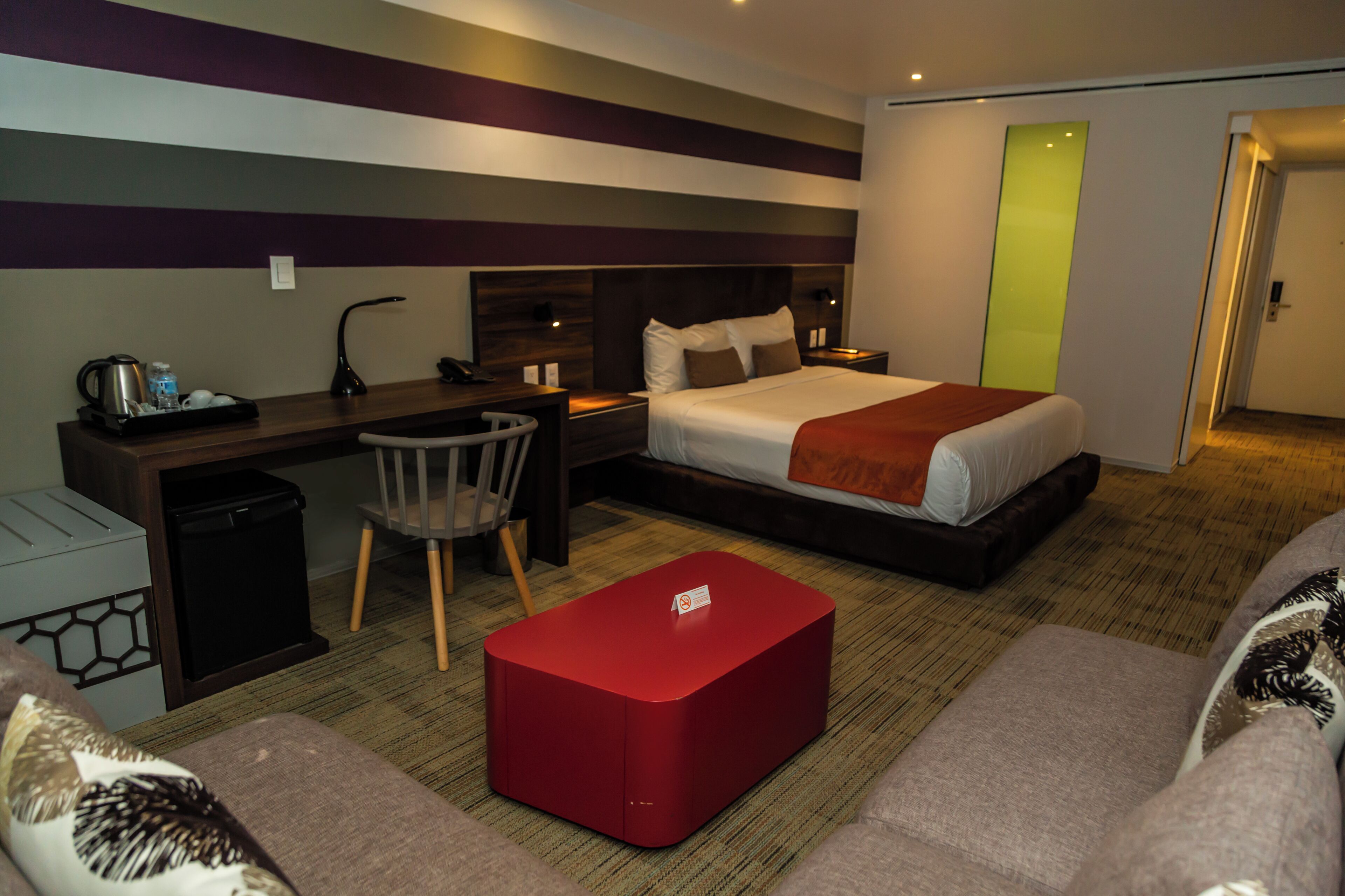 A hotel room with a bed, desk, chair, and ottoman.
