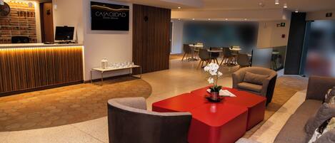 A hotel lobby with a reception desk, seating area, and a dining space.