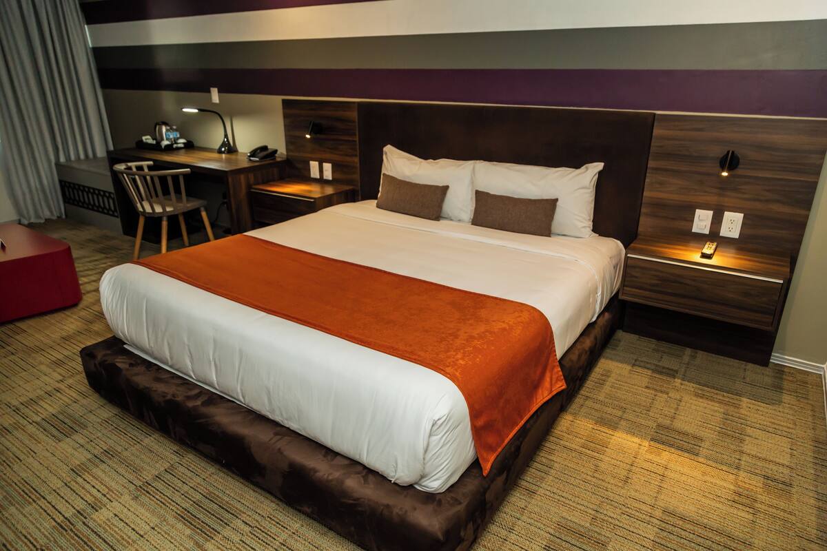 Una habitación de hotel con una cama grande, un escritorio, una silla y un reposapiés rojo.