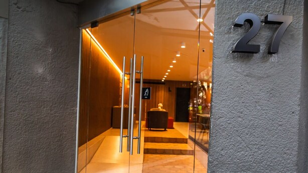 Entrada de hotel con puerta de vidrio, señal de accesibilidad para sillas de ruedas y el número 27 en la pared.