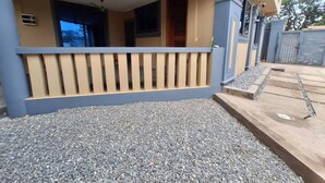 Een woongebouw met een overdekte veranda, een grindpad en een hekwerk.
