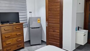 Hotelkamer met een bed, een houten dressoir, een koelkast, een houten kledingkast en een badkamer met wastafel en spiegel.