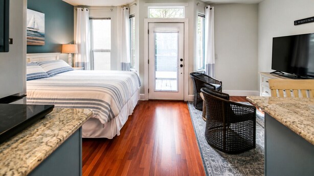 A bedroom with a bed, a TV, a desk, wicker chairs, and a door leading to a balcony. - Parkside Suite: Downtown Jacksonville (Jacksonville)