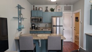 A kitchen with blue cabinets, a stainless steel refrigerator, and a microwave. There are two bar stools and a small island with a granite countertop. - Parkside Suite: Downtown Jacksonville (Jacksonville)