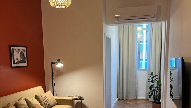 A living room with a sofa, a table, a lamp, a hanging light fixture, and a television. - Cozy apartment - Copacabana (Rio de Janeiro)