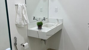 A bathroom with a white sink, a mirror, a towel rack, a toilet, and a shower. - Cozy apartment - Copacabana (Rio de Janeiro)