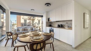 A modern kitchen with white cabinets, a dining area with a round table and chairs, and a balcony with a view of buildings. - Superb terrace apartment in Monaco-Beausoleil (Beausoleil)